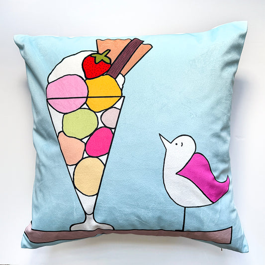 Square cushion of a pink winged seagull and icecream sundae with different coloured scoops, flake, strawberries, flake, wafer and cream. The background is a pale blue