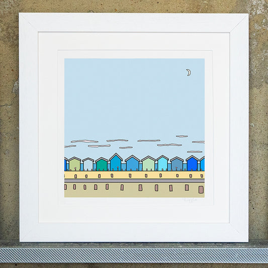Giclee original artwork print in a white mounted frame. Multiple beach huts are in a row with groynes that have three small pink winged seagulls. The beach huts are in shades of greens and blues on a sandy beach and a strip of blue for the sea in the background. Above the beach hut are thin streaky clouds and above a large pale blue sky with a small half moon in the top right corner. All the details, colours and shapes are outlined in thick black.
