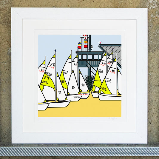 Giclee original artwork print in a white mounted frame. Six sailing boats with GBR are docked on a yellow sand coloured floor. In the background is a plant with wooden decking that has a pole of flags. There are steps leading up to the decked building and a small pink winged seagull is pearched on top of the wooden building.