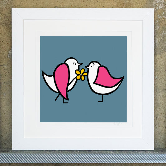 Giclee original artwork print in a white mounted frame. Original print called say it with flowers. Two pink winged seagulls are facing each other one is holding a yellow flower under its wing. The background is a blue teal.