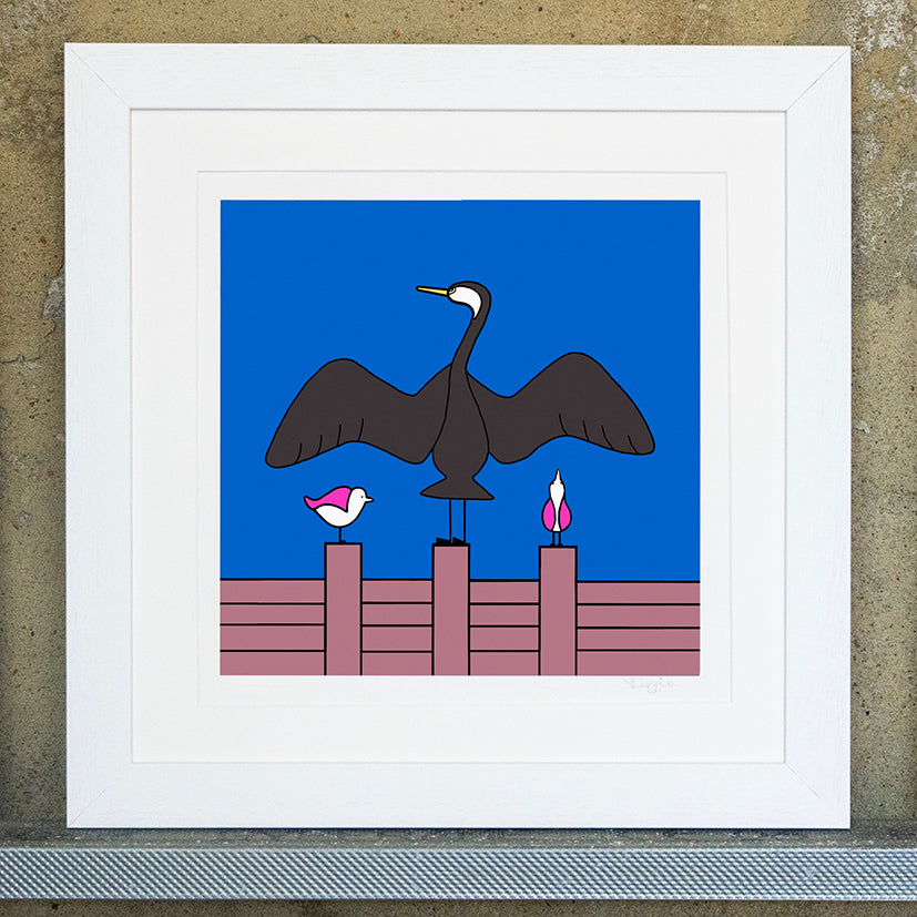 Giclee original artwork print in a white mounted frame. A groyne has a cormorant with it's wings spread out. Either side are two pink winged seagulls also perched on the groyne, one is looking up at the wing of the cormorant and the other to the side. the sky is bright blue.