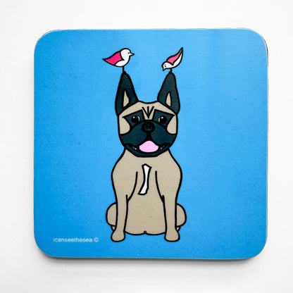 Coaster with a bright blue background, in the centre is a design of a brown beige dog with its pink tongue out. It's ears are pointed, with black and brown features on it's face, on its chest it has a little white patch. On top of it's pointy ears sits two pink winged seagulls looking in different directions. All the shapes and details are outlined in a fine line of black.