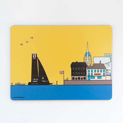 A placemat with a bright coloured design of old portsmouth. The sky is yellow with a bright blue sea, on the horizon is old portsmouth with the still and west pub, ben ainsley building in the background and the spinnaker tower behind the buildings. Two people are on the edge of the viewing point with a dog on a lead. In the sea is a black sailing boat and small cruiser. In the centre is a green boyd and three pink winged seagulls are flying across the sky.