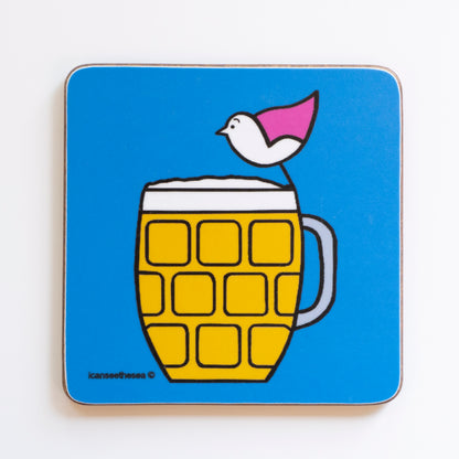 A coaster with a bright blue background. In the centre of the design is a large pint of beer in a mustard yellow colour with white at the top. On top of the beer sits a pink winged seagull on the rim looking across the beer. The pint glass has square indentations on it with a handle on the right handside. The shapes and details are outlined in black liner.