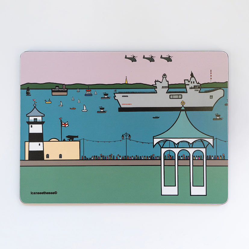 A placemat of southsea bandstand and the Queen Elizabeth air craft carrier. The colours are blues, greens and pinks. In the distance is the isle of wight in a green landscape, the sea is bright blue with small sailing and fishing boats. The sky is pink with three helicopters and in the sea the air craft carrier. On the sea's edge is a brick wall and little figures in different colours looking out. Southsea band stand sits at the front on a green field.