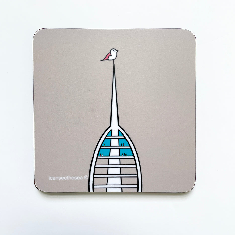 A coaster with a beige grey background. In the centre is the top half of the spinnaker tower with a few figures looking out of the glass floors. At the top of the point is a pink winged seagull perched on top looking out. The spinnaker tower is white with blue window glass.