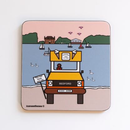 A coaster of a painting of bosham. An icream van in yellow and orange is parked facing forward. Next to the van is a post that says the road floods each tide. Behind the van is the sea in pale blue with swans and small sailing boats. The far distance is a green horizon with two buildings, in the pale peach sky flys three pink winged seagulls. All the details and shapes are outlined in black liner.