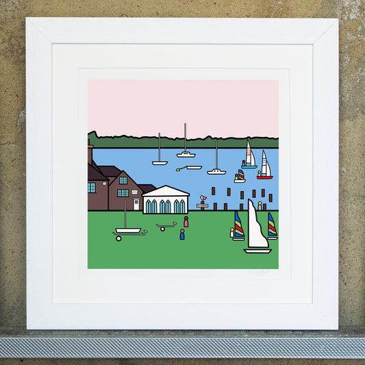 Giclee original artwork print in a white mounted frame. The print is of Bosham Sailing Club with a green grassy area with sails and trailers. A building can be found on the left infront of the sea with groynes and small boats in the distance. In the far distance is a green landscape with a pale pink sky. One groyne has a small pink winged seagull perched on top with a no parking sign.
