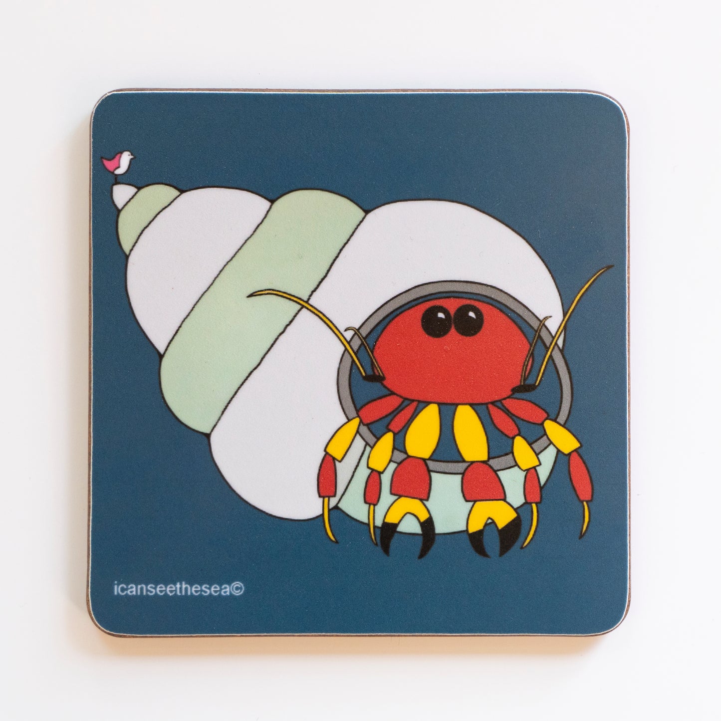 a coaster with a navy background of a painting of a hermit crab. The shell is stiped with pale green and pale blue. The crab is red and yellow with two black beady eyes. On the point of the shell is a pink winged seagull looking out. All the details and shapes are outlined in black.