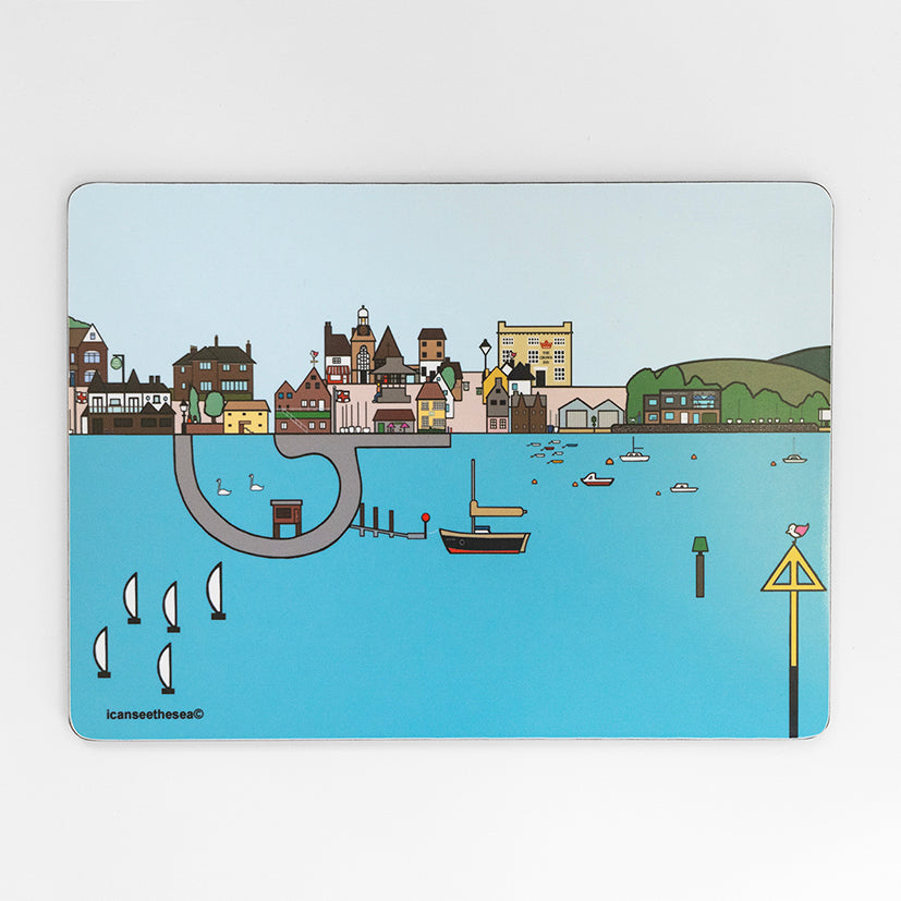 a placemat of a painting of emsworth. The water is pastel blue with sailing boats, swans, fishing boats and buoys. The horizon has lots of detailed buildings, streets, trees and a pub. The sky in the back ground is pale blue, and the water has a small area to walk round with swans. 