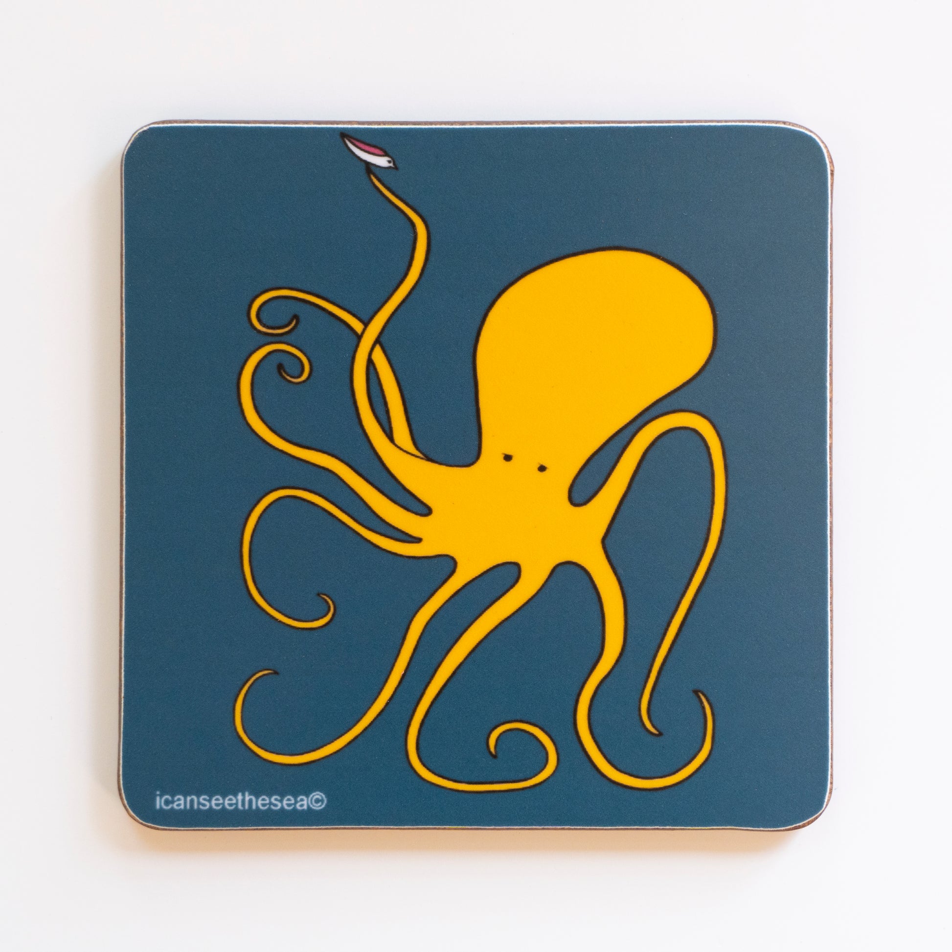 a coaster of a painting with a navy background. A golden yellow octopus with a pair of black eyes has a pink winged seagull sat on the end of its tentacle.