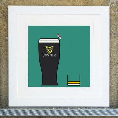 Giclee original artwork print in a white mounted frame. A pint of guiness and a small glass of whiskey are placed next to each other. The background is a bottle green colour. A small pink winged seagull is perched on the edge of the pint of guinness looking down at the whiskey.