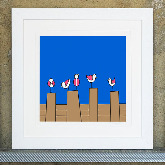 Giclee original artwork print in a white mounted frame. Five pink winged seagulls are perched on top of four groynes. Each seagull is looking in different directions. The background is a bright blue with brown groynes. The details and shapes are outlined in black. The print is called humble beginnings.