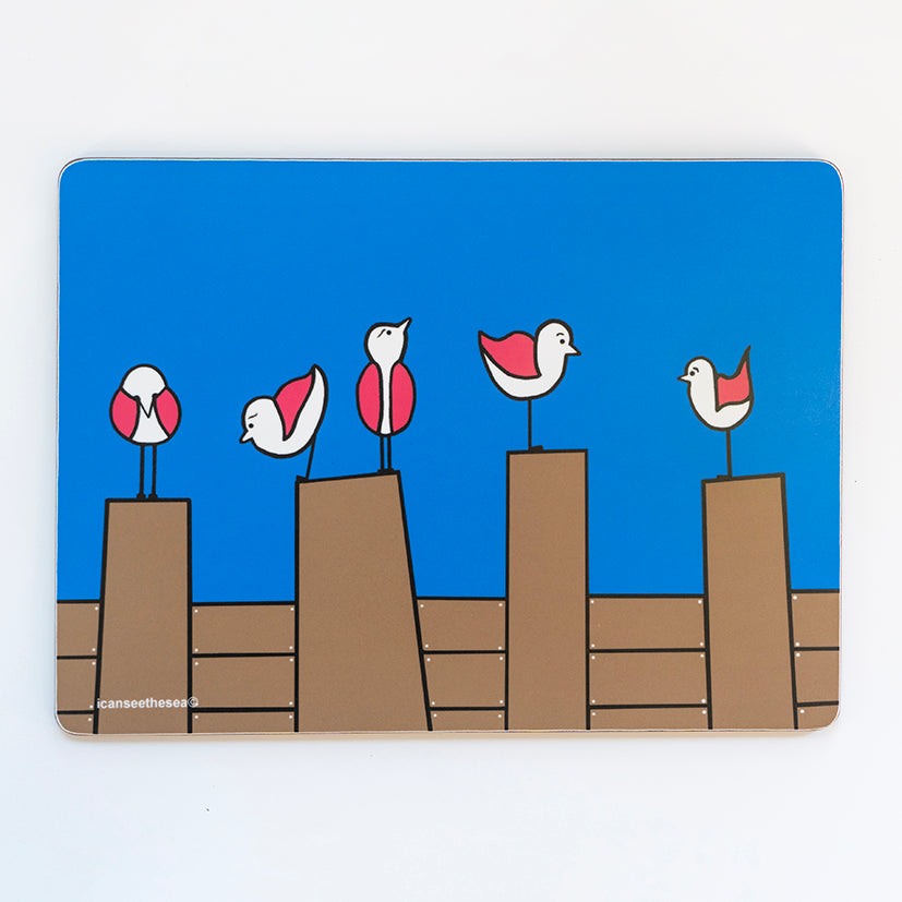 placemat from an original painting four pink wing seagulls are perched on three brown groynes with a bright blue background with icanseethesea text on the bottom left