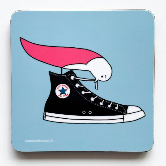 A pale blue coaster with a pink winged seagull stood in a black converse shoe tugging at a shoelace. The shapes and details are outlined in black line.