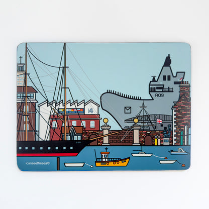 A blue placemat of a painting of Portsmouth Dockyard and the prince of wales carrier. The sea is bright blue with the warrior, small fishing boats and buoys. On the horizon is the main dockyard gate, wall, boathouse 4, porters lodge and sculpture. On top of one of the buildings sits a pink winged seagull on the chimney looking down. In the far distance is the prince of wales carrier in grey. The sky is pale blue.