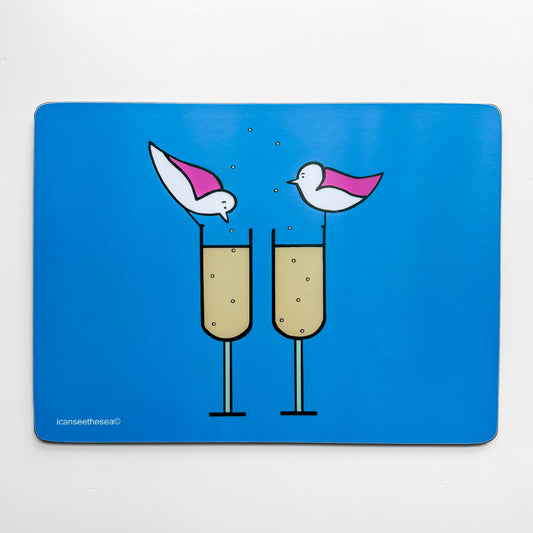 A bright blue placemat of a painting of champagne bubbles. Two champagne flutes are side by side with pale liquid and bubbles in the glass rising up out the top of the glass. Two pink winged seagulls are perched on each glass rim, one is looking down at the drink and the other looking across.